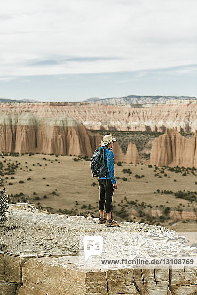 Wanderin in voller Länge mit Rucksack  die auf einer Felsformation stehend die Aussicht betrachtet
