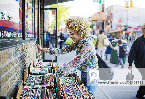 Side view of smiling woman searching for records outside store in city