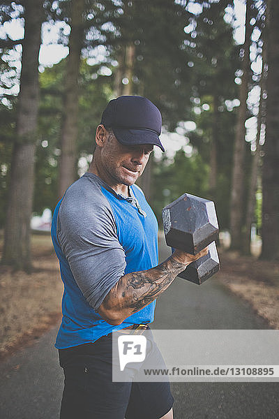 Side view of man lifting dumbbell while standing on road at park