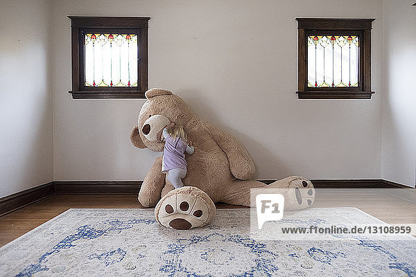 Mädchen spielt zu Hause mit großem Teddybär an der Wand
