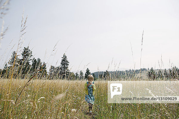 Girl walking on grassy field against clear sky