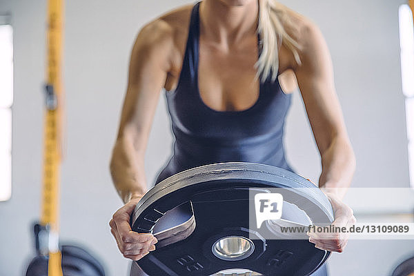 Midsection of woman lifting weight plate while exercising in gym