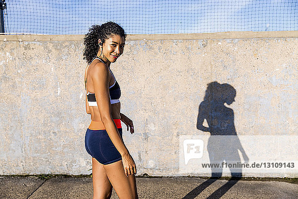 Porträt einer Sportlerin  die sich im Stehen auf einem Fußweg an der Wand bewegt