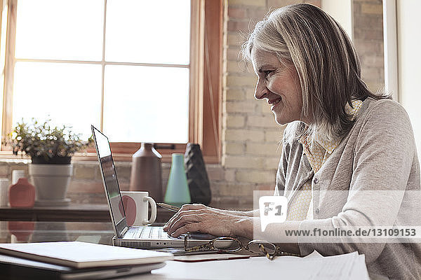 Side view of smiling businesswoman using laptop in creative office