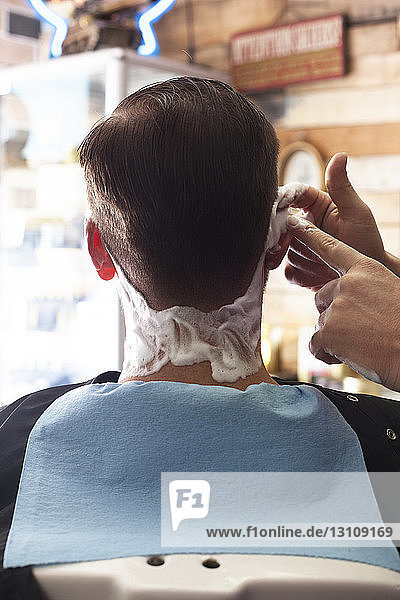 Ausgeschnittenes Bild eines Barbiers  der Rasierschaum auf den Kunden aufträgt
