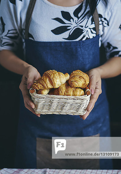 Midsection of woman holding croissants in basket at kitchen