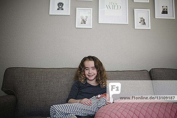 Portrait of cheerful girl with sister sitting on sofa at home