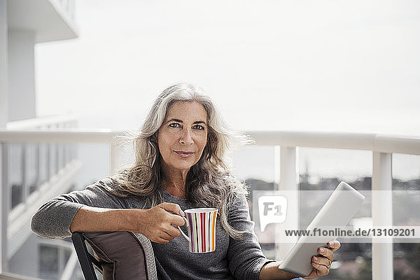 Porträt einer selbstbewussten reifen Frau mit Tablet-Computer und Kaffeetasse auf dem Balkon