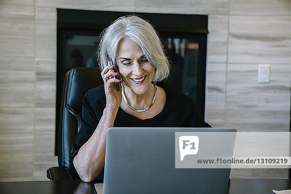 Lächelnde Geschäftsfrau beantwortet Smartphone  während sie im Büro sitzt