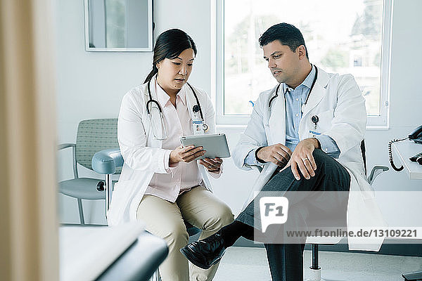 Doctors discussing over tablet computer while sitting in examination room