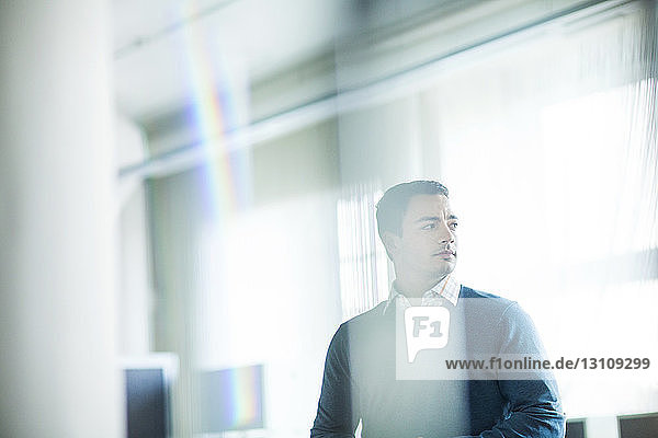 Thoughtful man standing in office seen through glass window
