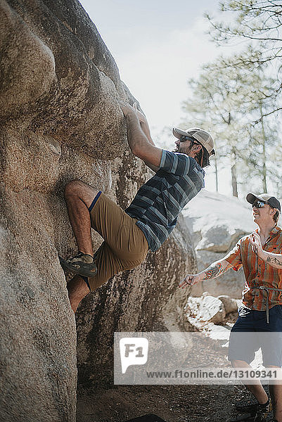 Man assisting friend in climbing rock against sky at forest