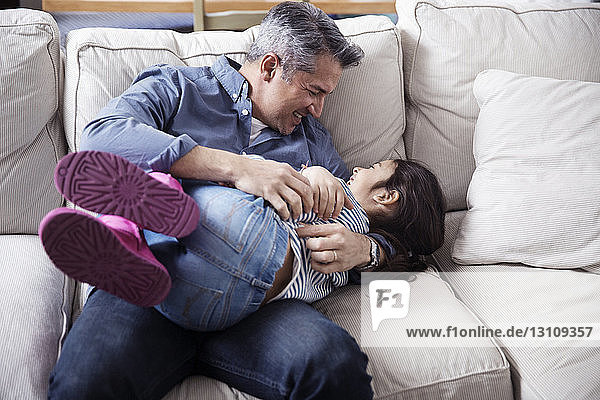Fröhlicher Vater und Tochter genießen zu Hause auf dem Sofa