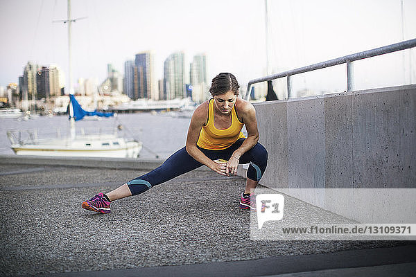 Female athlete stretching leg on pier by harbor
