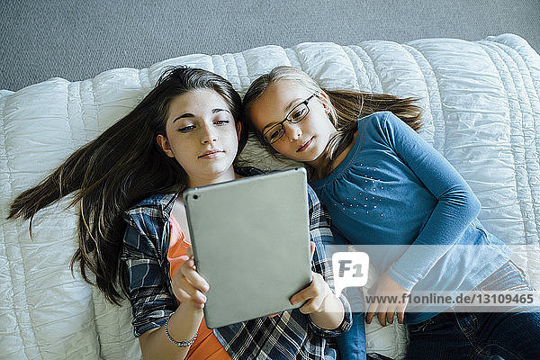 Hochwinkelansicht von Schwestern mit einem Tablet-Computer  während sie zu Hause auf dem Bett liegen