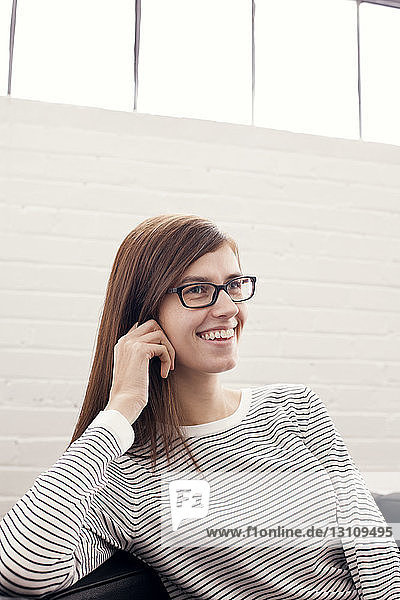 Lächelnde Geschäftsfrau sitzt im Büro an der Wand