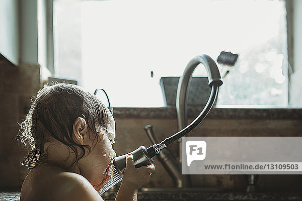 Nahaufnahme eines Mädchens  das mit dem Wasserhahn spielt  während es zu Hause am Fenster in der Küchenspüle sitzt