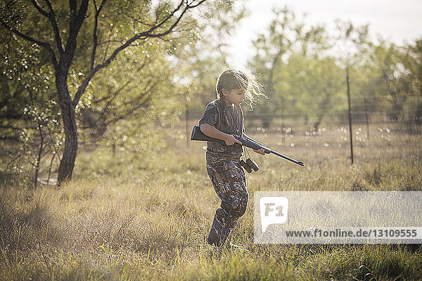 Girl holding rifle while walking on grassy field