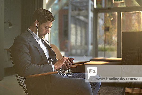 Businessman using mobile phone while sitting on chair in office