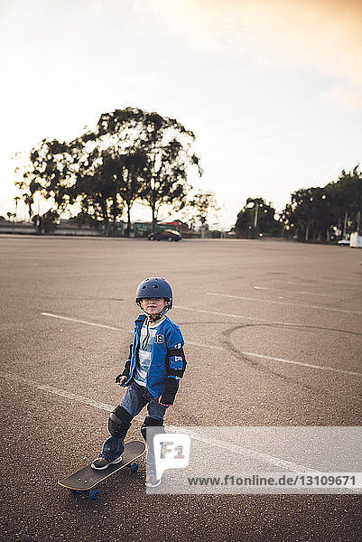 Porträt eines süßen Jungen  der mit Skateboard auf dem Feld vor klarem Himmel steht