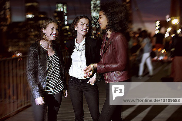 Happy friends talking while standing on street at night