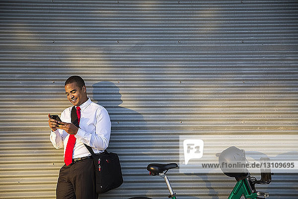 Smiling businessman using mobile phone while standing against closed shutter