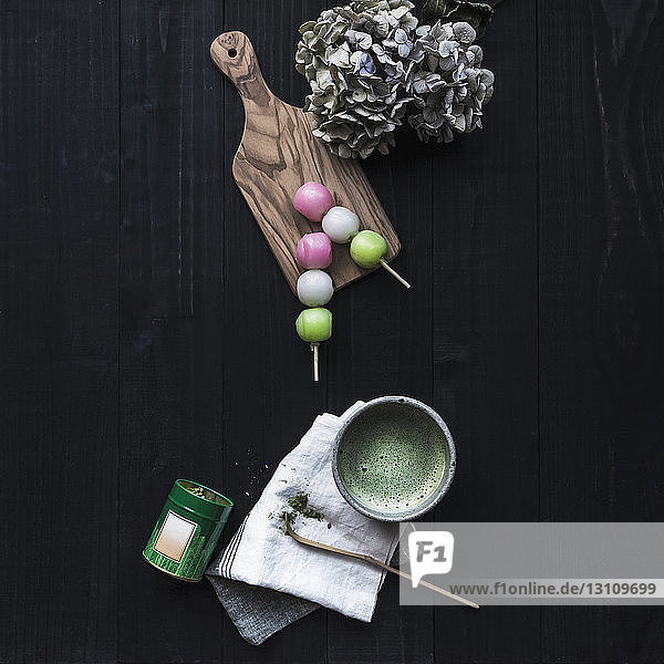 Draufsicht auf Matcha-Tee mit Süßspeisen und Hortensien auf schwarzem Tisch