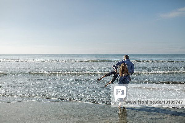 Playful father carrying daughter while walking towards sea at beach
