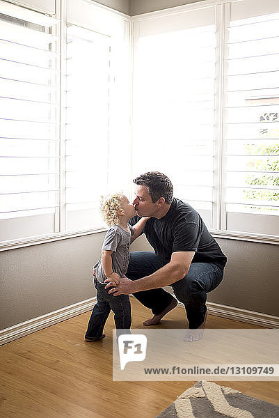 Vater und Sohn küssen sich zu Hause auf Mund gegen Fenster
