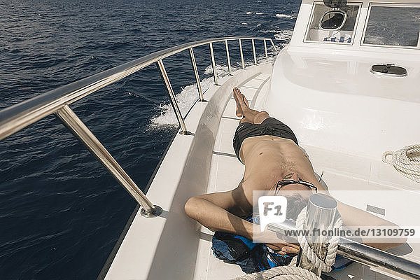Hochwinkelaufnahme eines Mannes ohne Hemd  der bei Sonnenschein auf einer Yacht auf dem Meer liegt