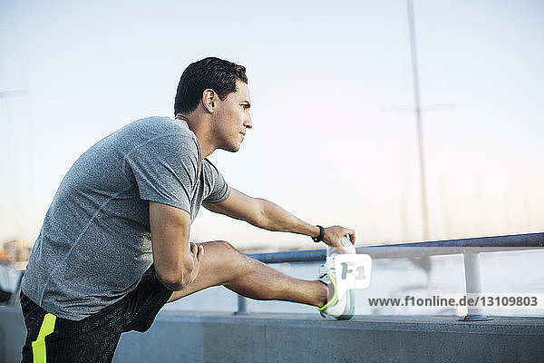 Nachdenklicher männlicher Athlet streckt Bein auf Pier am Hafen