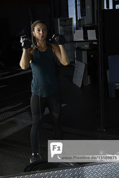 Reflektion einer Frau  die beim Hanteltraining im Fitnessstudio Hanteln hebt  im Spiegel betrachtet