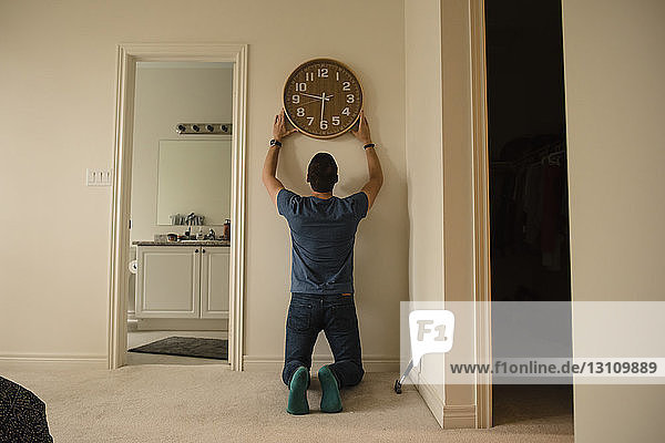 Rückansicht eines Mannes  der zu Hause eine Uhr an der Wand befestigt