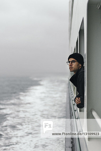 Nachdenklicher Mann schaut durch ein Fenster  während er auf einem Kreuzfahrtschiff reist