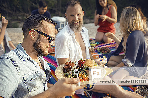 Mann isst mit Freunden am Strand