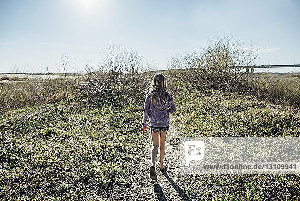 Rückansicht eines Mädchens  das am sonnigen Tag auf dem Feld gegen den Himmel läuft