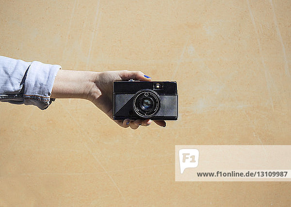 Cropped image of woman holding camera against wall