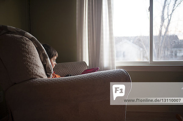 Junge spielt mit Spielzeug  während er auf einem Stuhl am Fenster sitzt