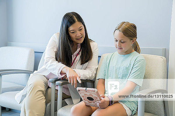 Kinderarzt betrachtet Mädchen mit Tablet-Computer im Krankenhaus