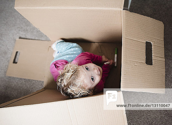 High angle view of playful girl sitting in cardboard box at home