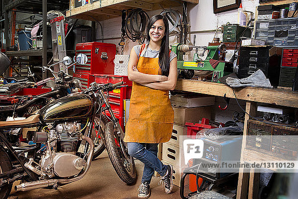 Porträt einer glücklichen Mechanikerin mit verschränkten Armen  die in der Werkstatt steht