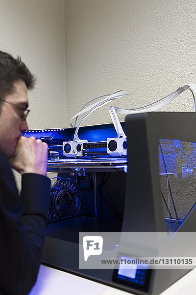 Männlicher Ingenieur bedient 3D-Drucker auf Tisch im Büro