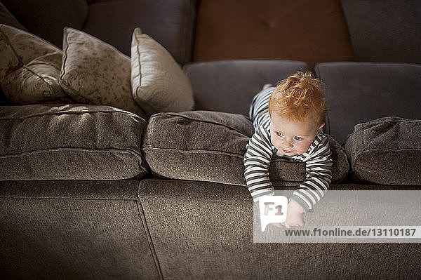Hochwinkelansicht eines süßen kleinen Jungen  der wegschaut  während er zu Hause auf dem Sofa steht