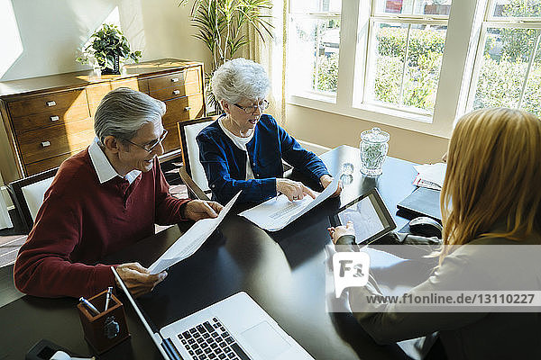 Schrägansicht eines älteren Ehepaares beim Lesen von Dokumenten während einer Diskussion mit einem Finanzberater im Amt