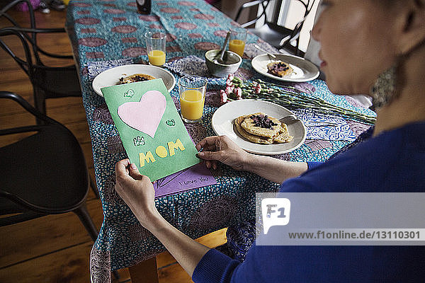 Hochwinkelansicht einer Frau  die am Geburtstag am Esstisch eine Glückwunschkarte hält