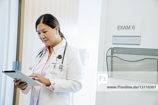 Ärztin  die einen Tablet-Computer benutzt  während sie im Krankenhaus an der Wand steht