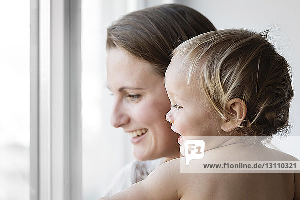 Side view of happy mother with daughter looking through window at home