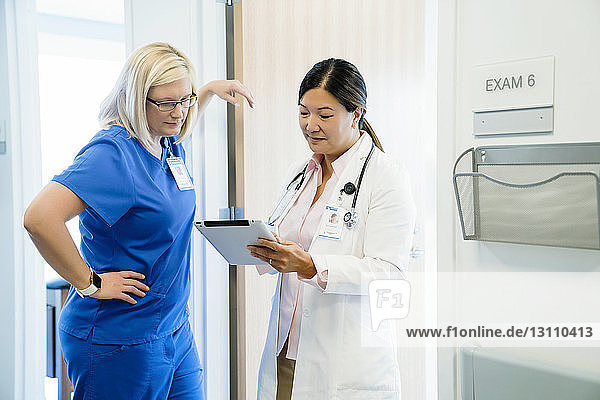 Female doctors looking at tablet computer while standing by wall in hospital