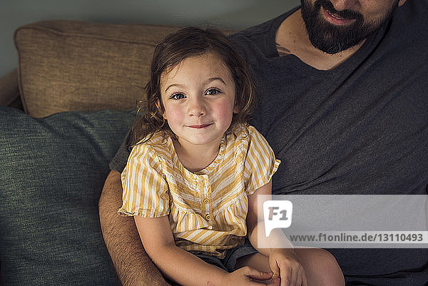 Hochwinkelporträt eines Mädchens  das mit seinem Vater zu Hause auf dem Sofa sitzt