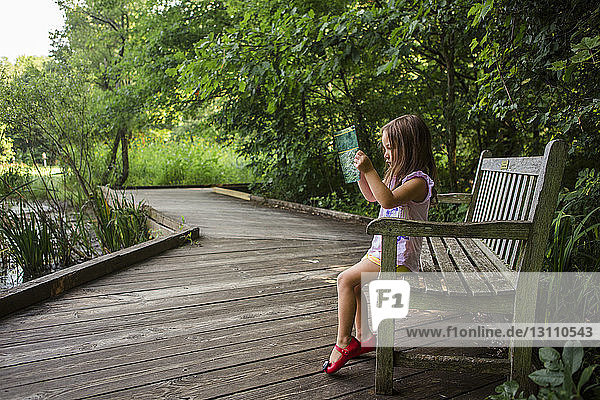 Seitenansicht eines Mädchens  das auf einer Parkbank sitzend ein Buch liest
